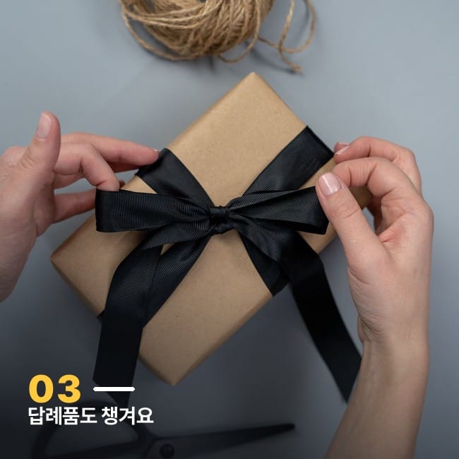 크래프트지로 포장하고 검은 리본을 묶는 손